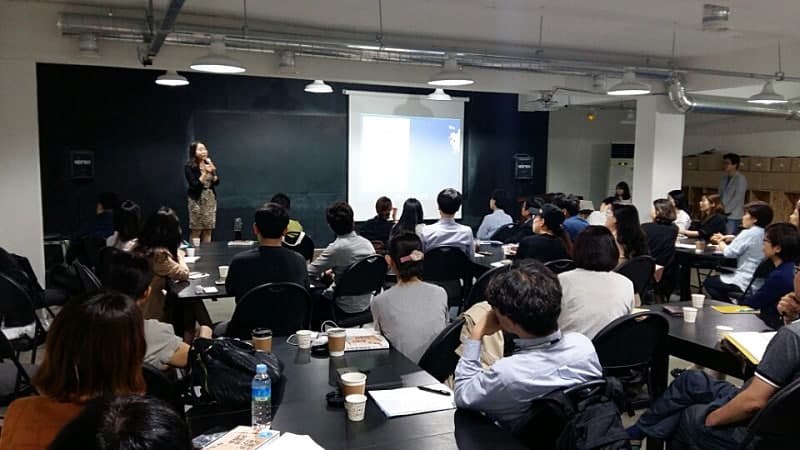 강연장을 가득 채운 청중이 강연자의 이야기를 듣고 있는 모습